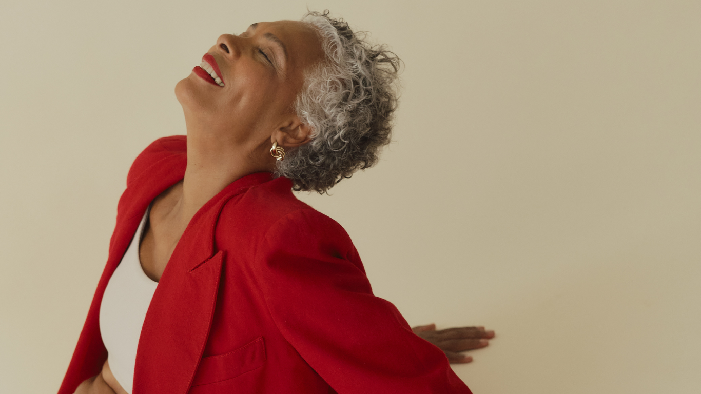 Older black woman sitting with gray hair in a red blazer and white shirt